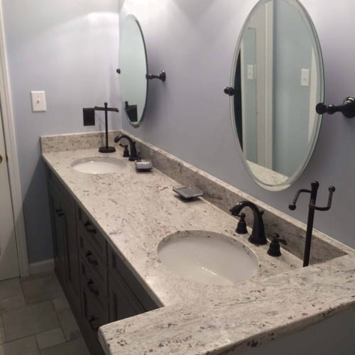 Modern bathroom vanity with granite countertop, dual oval mirrors, black fixtures, and stylish lighting, showcasing professional bathroom renovation by My Contracting Guy.