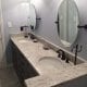 Modern bathroom vanity with granite countertop, dual oval mirrors, black fixtures, and stylish lighting, showcasing professional bathroom renovation by My Contracting Guy.