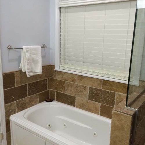 Modern bathroom with a whirlpool tub, beige stone tile accents, and white window blinds, showcasing professional bathroom remodeling services by My Contracting Guy.