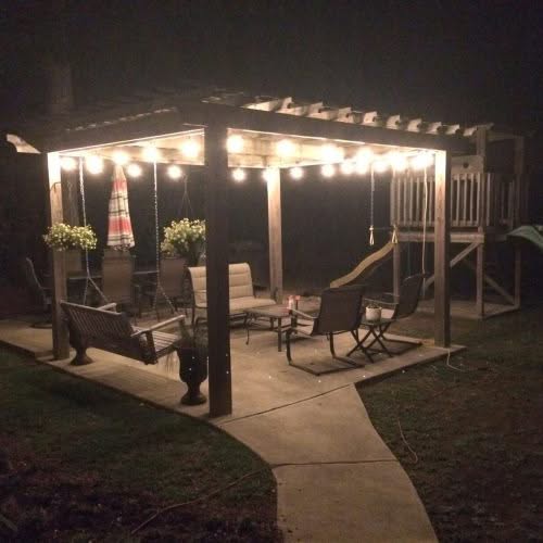 String lights illuminating a backyard patio with seating, a swing, and a playset; perfect for outdoor entertainment and backyard remodeling projects.