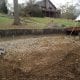 Excavation and foundation preparation for landscaping or construction on a residential property with existing structures and mature trees.