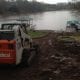 Heavy construction equipment working near a flooded waterfront property, highlighting flood mitigation, lake restoration, and property repair services.