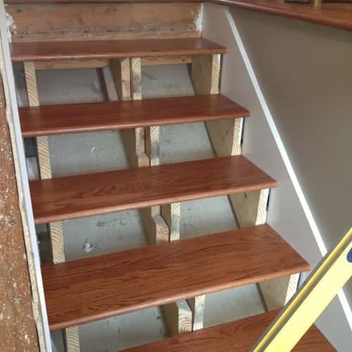 Newly installed wooden staircase steps with a dark stain finish, supported by light-colored framing, in the process of renovation or construction.
