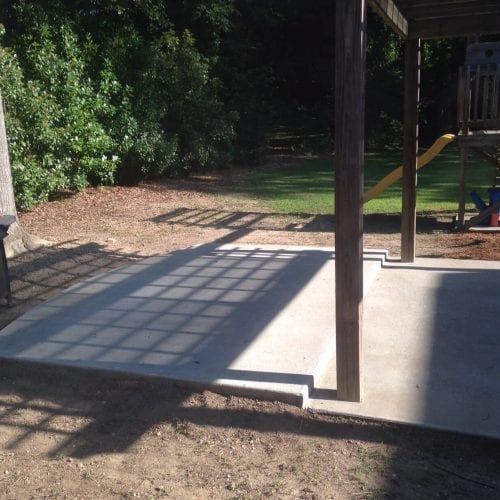 Modern concrete patio with a wooden deck and playground equipment, ideal for outdoor family activities and relaxation, custom-built by My Contracting Guy.